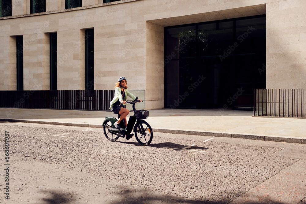 Businesswoman commuting through electric bicycle on road near building Businesswoman commuting through electric bicycle on road near building