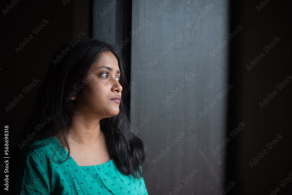 Young woman wearing green dress looking outside through window Young woman wearing green dress looking outside through window