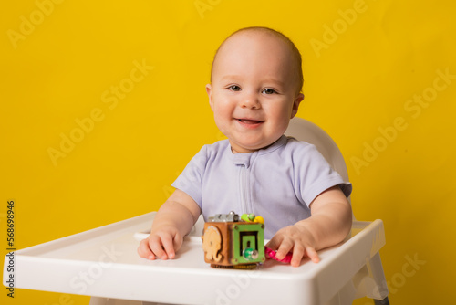 a cute kid is sitting in a child's chair playing with an educational wooden toy on a yellow background. bizi-board