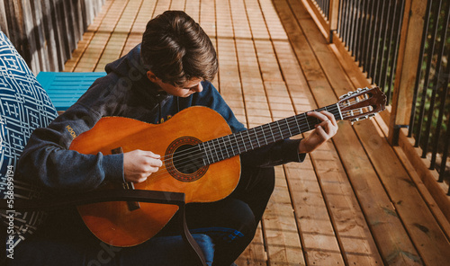 Teen boy playing an acoustic guitar on the deck of a log home. photo
