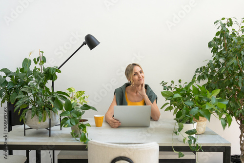 Thoughtful freelancer sitting with laptop at desk photo