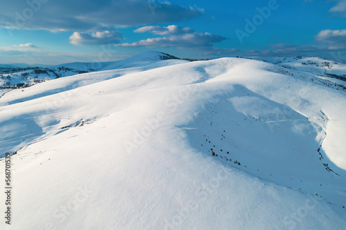 Aerial shot of snow-capped hill top lit by the setting sun in winter sunset at Zlatibor, Serbia from drone pov.