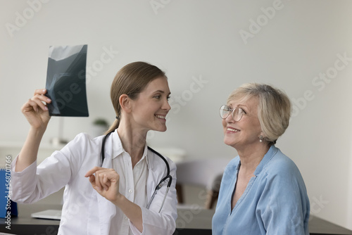 Photos Happy doctor woman showing Xray scan to elder patient, explaining shot of bones, radiography screening film to senior woman in hospital office