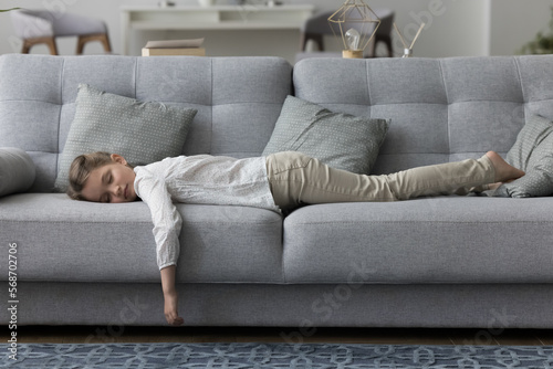 Calm sleepy little kid girl lying on belly, resting on comfortable soft couch with closed eyes, sleeping at daytime. Tired exhausted child taking break in home living room