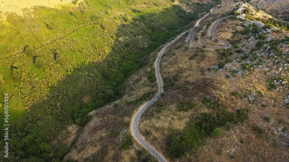 Drone shot of curvy mountain road in Corfu, Greece. Top down view to horizontal, panoramic view of the mountain top soaked in the sunset light. Drone shot of curvy mountain road in Corfu, Greece. Top down view to horizontal, panoramic view of the mountain top soaked in the sunset light.
