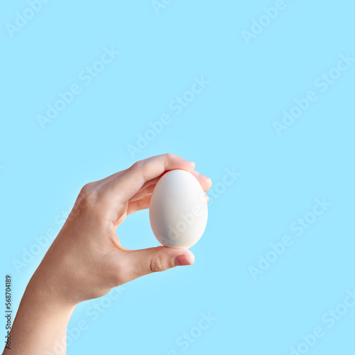 Minimalist Easter greeting, advertising or promotion card design, white egg in a hand on blue background, food market mockup with copy space
