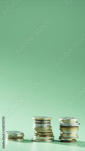 Three stacks towers of different coins appearing on green background, arranging growing graph. Money business, investment, savings economy, income, growth, market, success. Vertical. Stop motion.