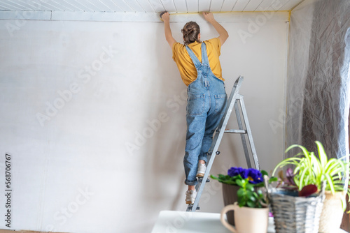 Young adult happy woman renovating the house, covering the walls with film before painting