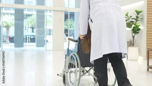 Doctor wheeling patient in wheelchair through lobby of Hospital.