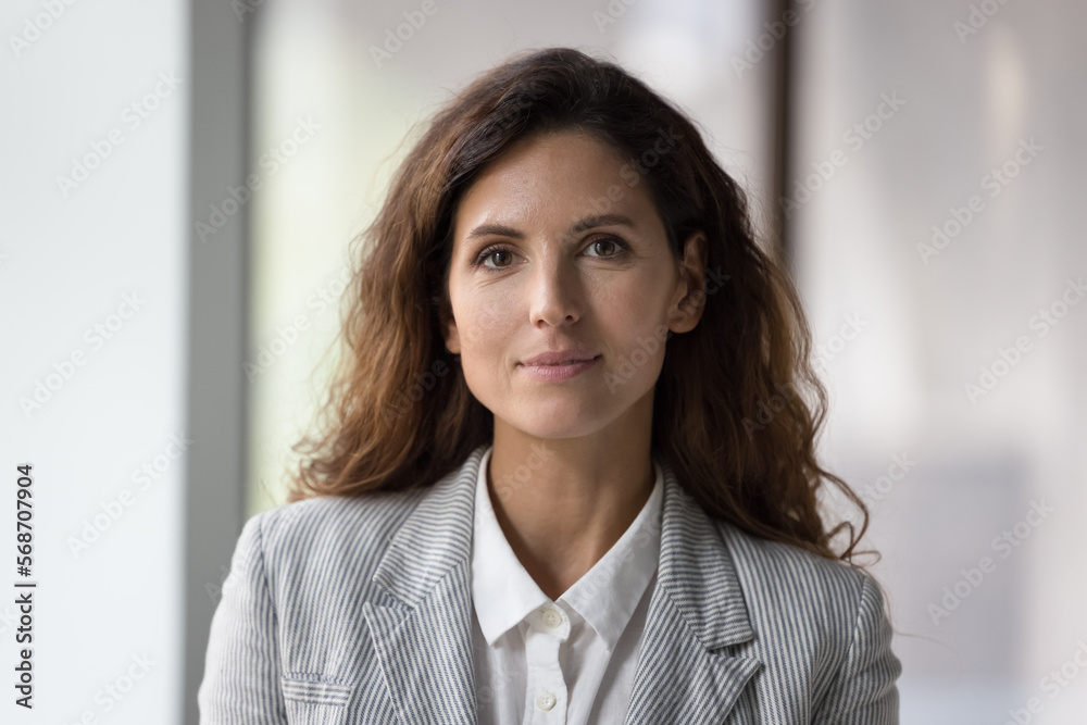 Positive beautiful millennial young businesswoman head shot face portrait. Confident pretty middle aged woman with black wavy hair, female business leader, company owner looking at camera, smiling Positive beautiful millennial young businesswoman head shot face portrait. Confident pretty middle aged woman with black wavy hair, female business leader, company owner looking at camera, smiling