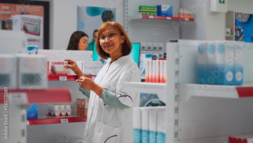 Female pharmacist arranging medical products on store shelves  preparing to help customers. Asian consultant looking at boxes of medicaments and vitamins  checking pills packages.