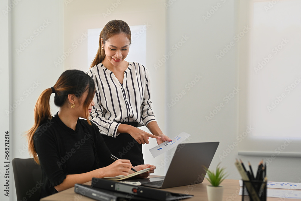 Attractive woman manager pointing at documents and explaining new strategies to coworkers during meeting in office Attractive woman manager pointing at documents and explaining new strategies to coworkers during meeting in office