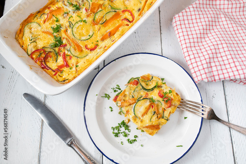 Frittata with mediterranean vegetables such as tomatoes, carrots, zucchini, onions, bell peppers and herbs in a baking dish on white background. Flat lay