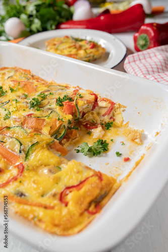 Oven baked frittata with mediterranean vegetables in a white baking dish on kitchen table.