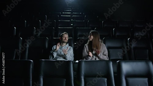 A young couple applauds after watching a movie at the cinema and leaves the cinema hall. An excellent premiere of the film took place