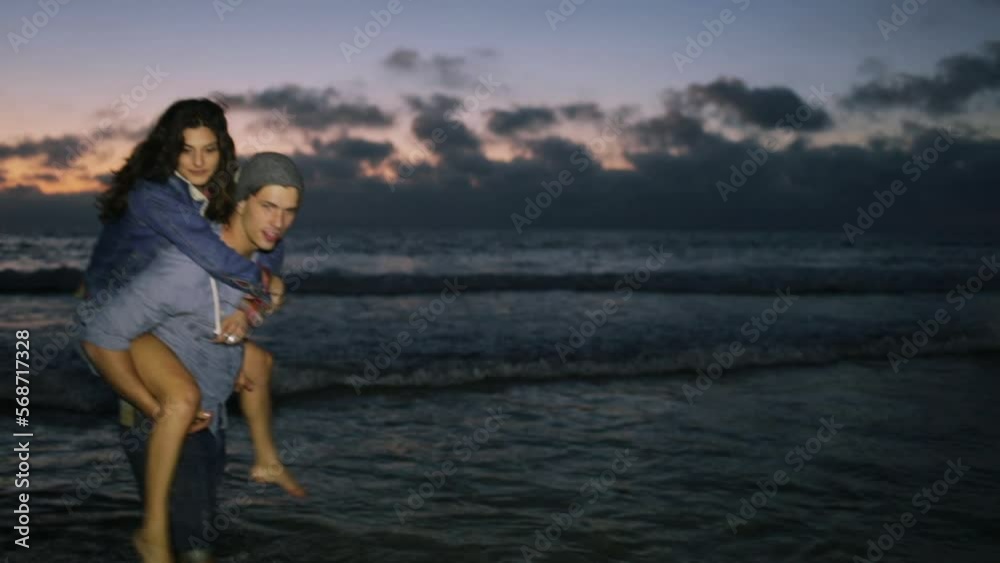 Man gives piggy back ride to woman while standing in ocean surf Man gives piggy back ride to woman while standing in ocean surf