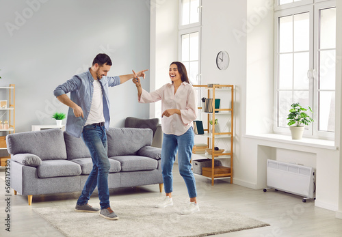 Happy overjoyed laughing young couple homeowners having fun dancing at home in living room celebrating moving into new apartment or enjoying a good mood. People, couple and family concept.