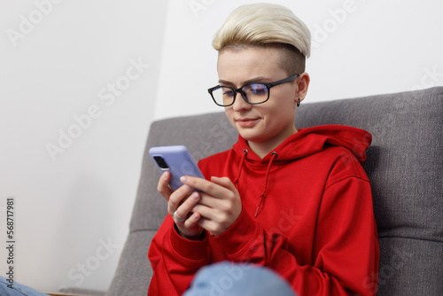 Young woman with short hair browsing mobile app on a smart phone. Stylish tom boy female person using modern mobile phone at home