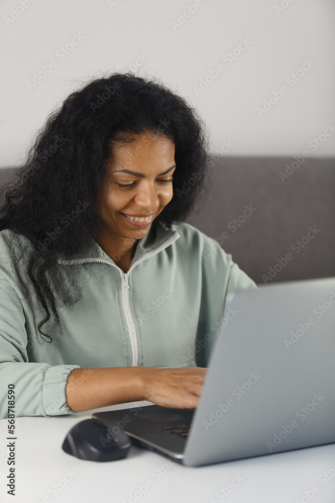 Happy African woman working on modern laptop computer at home. Cheerful BIPOC female typing text on modern notebook pc Happy African woman working on modern laptop computer at home. Cheerful BIPOC female typing text on modern notebook pc