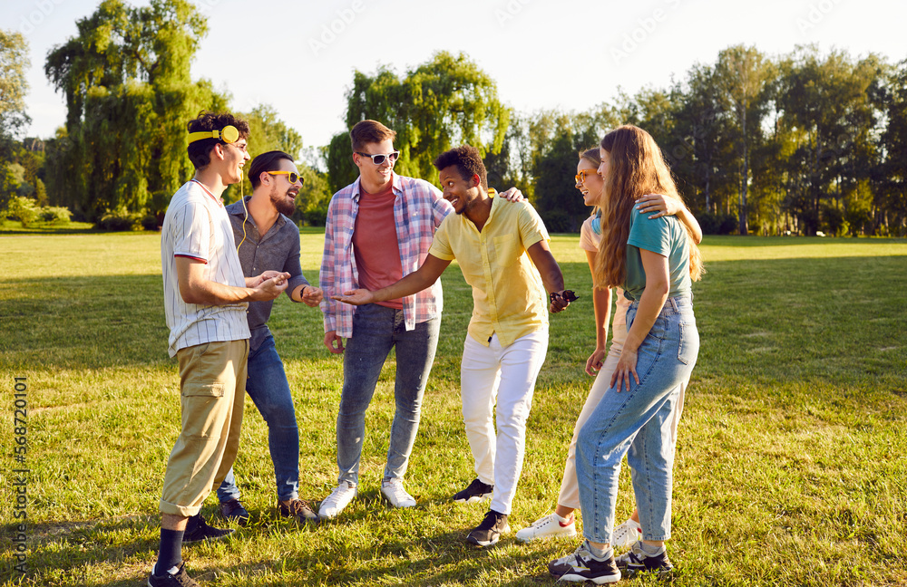 Group of happy multiracial friends having fun on warm summer day. Six young multiethnic people spending time outside, enjoying good weather, walking in clean green park, and having good time together Group of happy multiracial friends having fun on warm summer day. Six young multiethnic people spending time outside, enjoying good weather, walking in clean green park, and having good time together