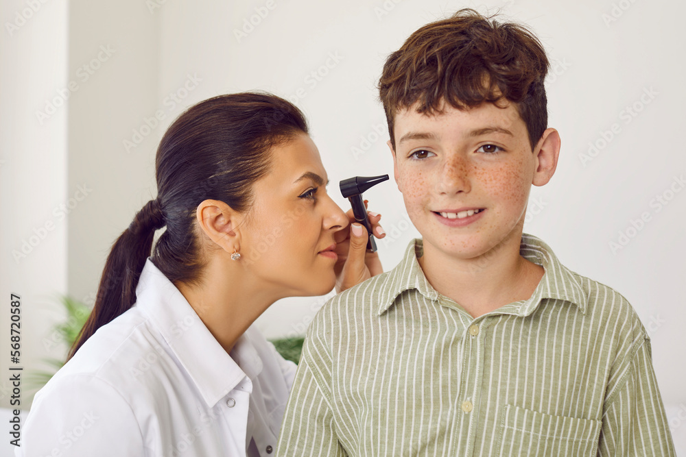 Specialist doing an ENT examination. Happy freckled school boy getting an ear checkup at the doctor's office. Professional otolaryngologist uses an otoscope to check ears of a little child Specialist doing an ENT examination. Happy freckled school boy getting an ear checkup at the doctor's office. Professional otolaryngologist uses an otoscope to check ears of a little child
