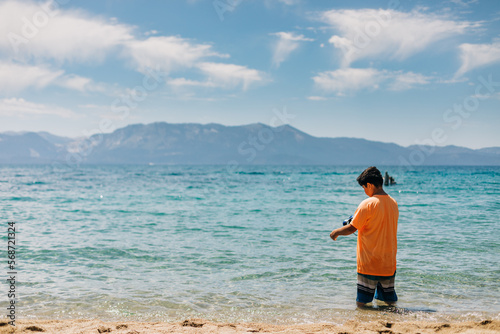 Kid Stands in a Mountain Lake with Blue Sky and Clouds