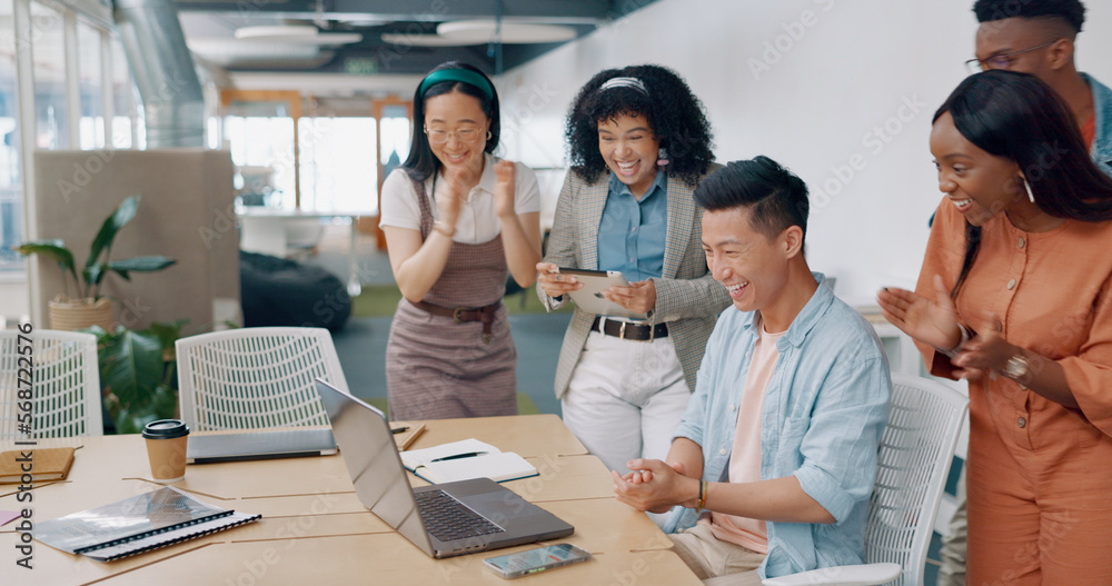 Fototapeta premium Winner, yes and applause with a business asian man cheering with his team while working on a laptop on his office. Goal, wow and success with a male employee and colleague group in celebration
