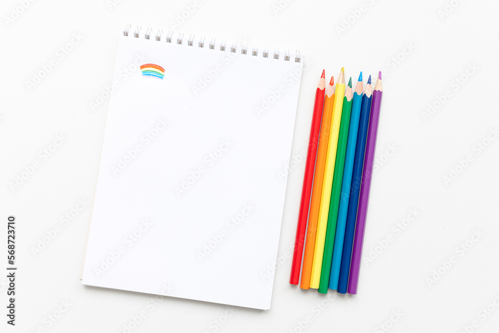 Top view Minimal design of open Notebook with colored pencils of rainbow colors on white background with blank space. Flat lay Top view Minimal design of open Notebook with colored pencils of rainbow colors on white background with blank space. Flat lay