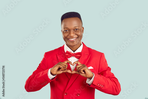 Handsome adult Afro American man in red suit makes hand heart shape. Benevolent human gentleman philanthropist businessman benefactor charity fund founder donates money wishes healthy life and harmony