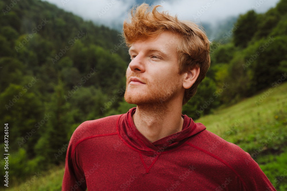 Young ginger man looking away while standing in mountains Young ginger man looking away while standing in mountains