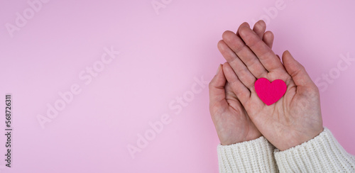 Woman's hands hold a pink heart on a pink background.Valentine's Day composition. Banner. Place for text. Top view. Selective focus.
