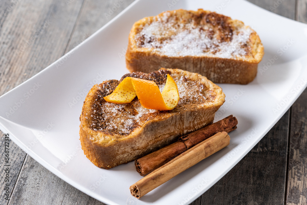 Traditional homemade Spanish torrijas decorated with cinnamon and Orange peel on wooden table Traditional homemade Spanish torrijas decorated with cinnamon and Orange peel on wooden table