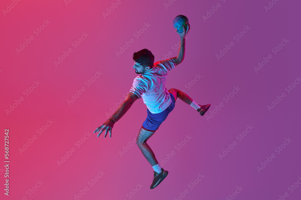Top view. In a jump. Young man, professional handball player training, playing isolated over gradient pink background in neon light. Winner. Concept of sport, action, championship, sportive lifestyle
