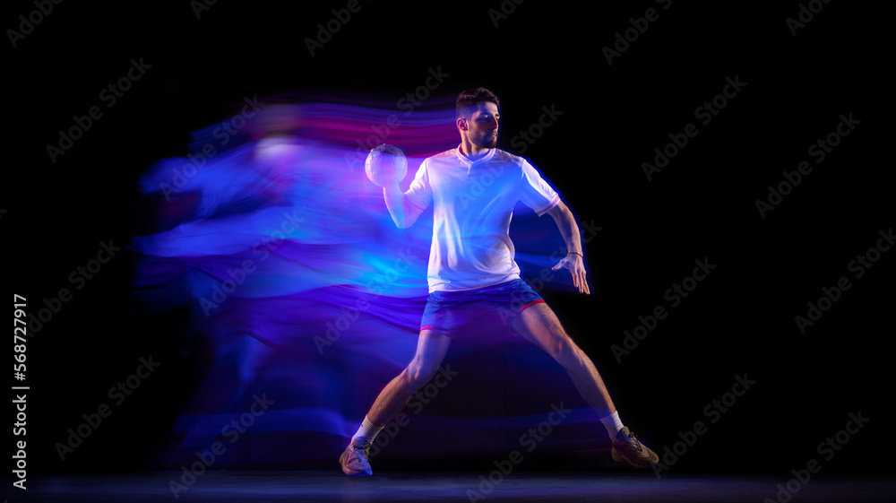 Power. Young man, professional handball player in motion, playing over black background with mixed lights effect. Concept of sport, action, motion, competition, championship, sportive lifestyle
