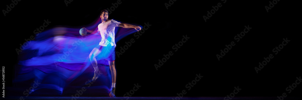 Young man, professional handball player in motion, playing over black background with mixed lights effect. Sport, motion, championship, sportive lifestyle concept. Banner, flyer. Copy space for ad
