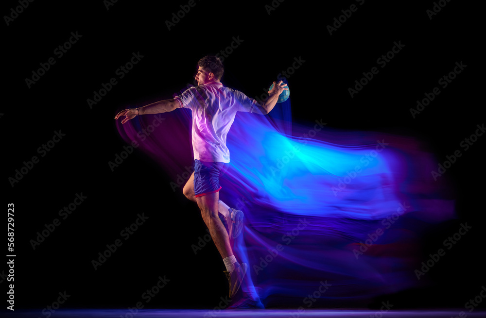 Side view. Winning goal. Young man, professional handball player in motion, playing over black background with mixed lights effect. Concept of sport, action, motion, championship, sportive lifestyle Side view. Winning goal. Young man, professional handball player in motion, playing over black background with mixed lights effect. Concept of sport, action, motion, championship, sportive lifestyle