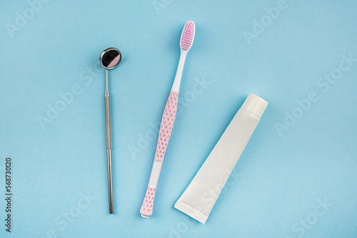 A set for oral care. Pink toothbrush, toothpaste and dental mirror on a blue background. The concept of dentistry and healthcare. Top view, flat position.  Copy space for text