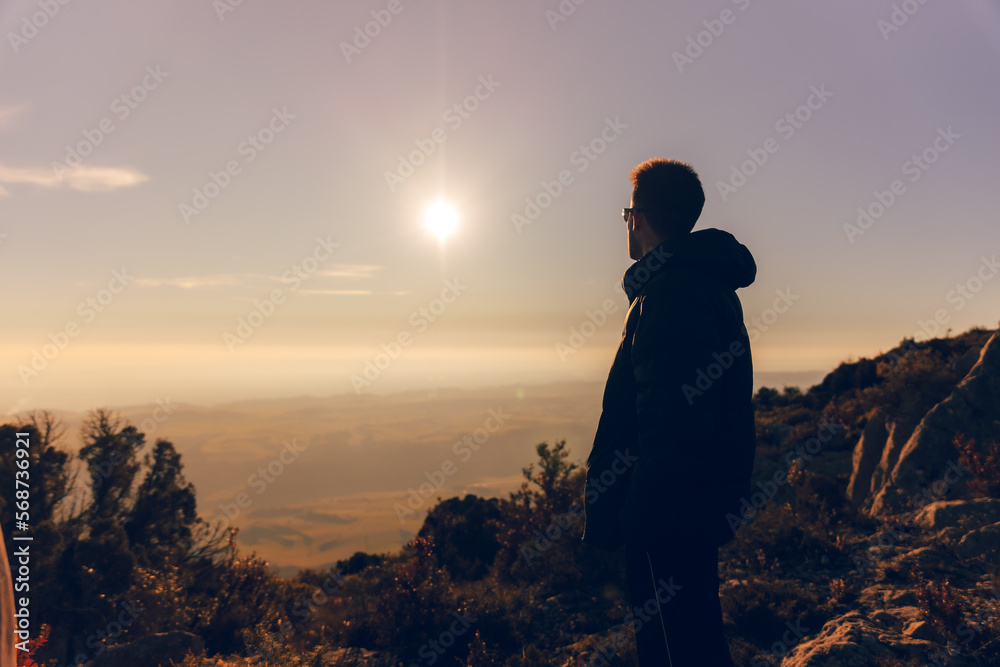 unrecognizable silhouette of young digital nomad adventurer bundled up watching the sunset with glasses