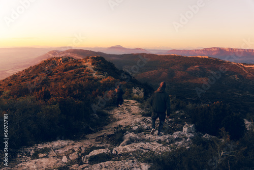Couple walking on top of the mountain on a stone path watching a beautiful sunset with orange and pink sky