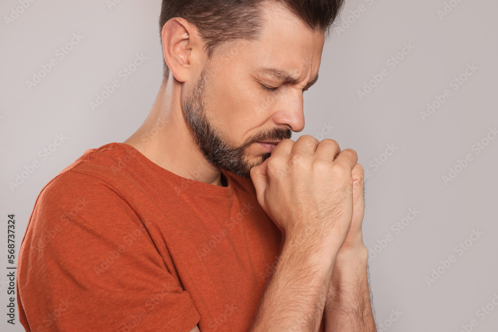 Man with clasped hands praying on light grey background, closeup Man with clasped hands praying on light grey background, closeup