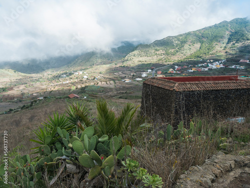 Old stone house at lush green valley with terraced fields and village Las Portelas. Landscape with rocks and hills seen from hiking trail at Park rural de Teno, Tenerife, Canary Islands, Spain. photo