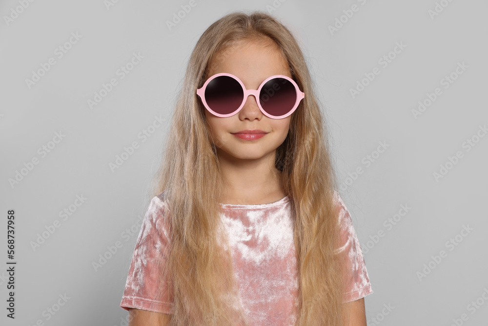 Girl in stylish sunglasses on light grey background