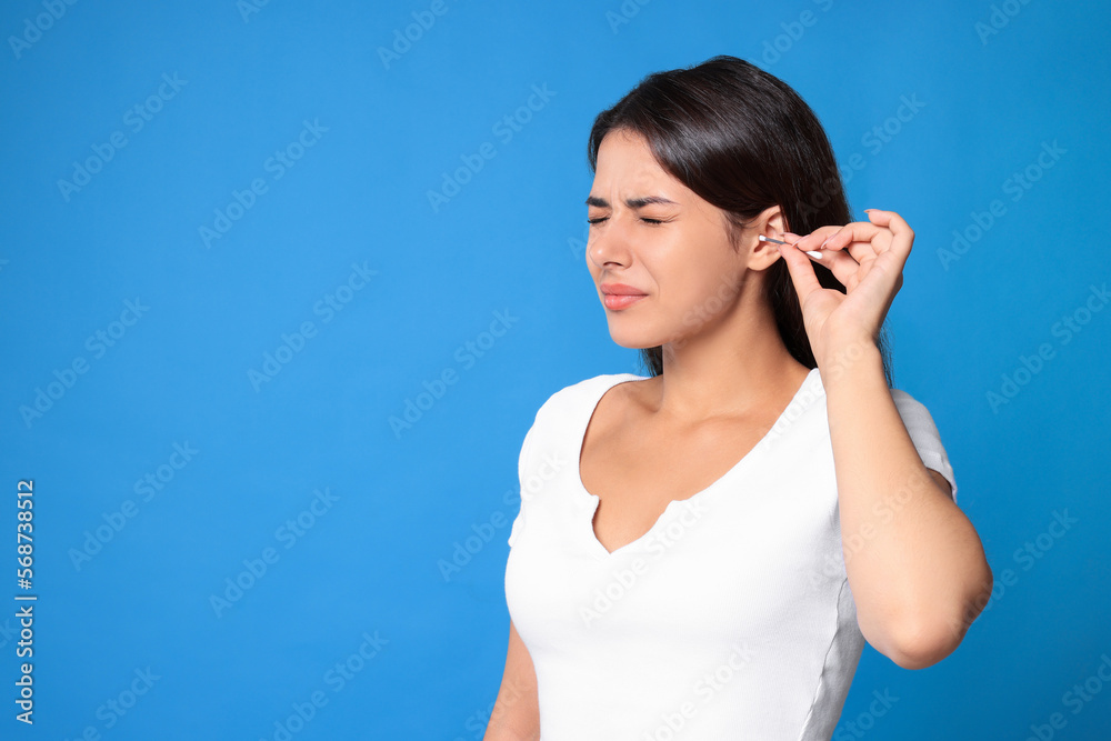 Young woman cleaning ear with cotton swab on light blue background, space for text Young woman cleaning ear with cotton swab on light blue background, space for text