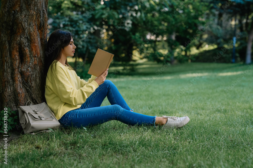 Young woman reading book near tree in park