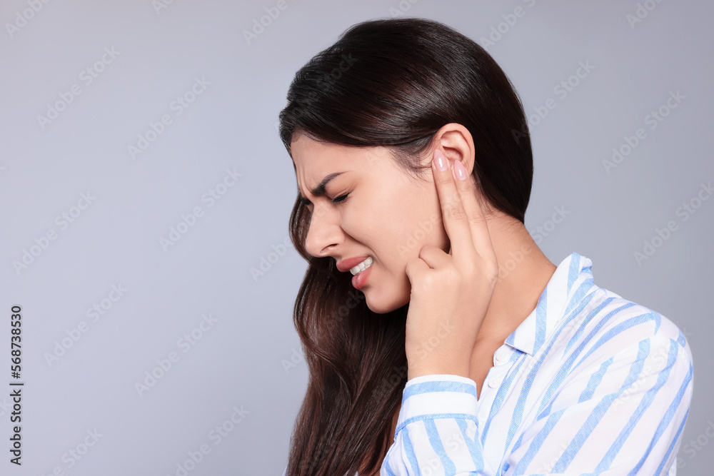 Young woman suffering from ear pain on light grey background, space for text Young woman suffering from ear pain on light grey background, space for text
