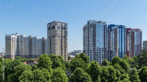 View from window on multi-storey multi-apartment residential complexes. High-rise residential buildings against blue spring sky. Park areas for recreation and walks. Krasnodar, Russia - May 26, 2022