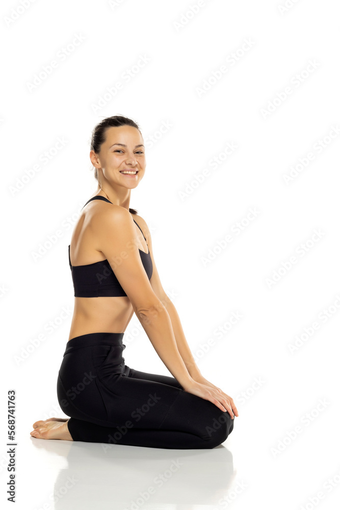 a young beautiful woman in black sportswear is resting sitting on the floor on a white background a young beautiful woman in black sportswear is resting sitting on the floor on a white background