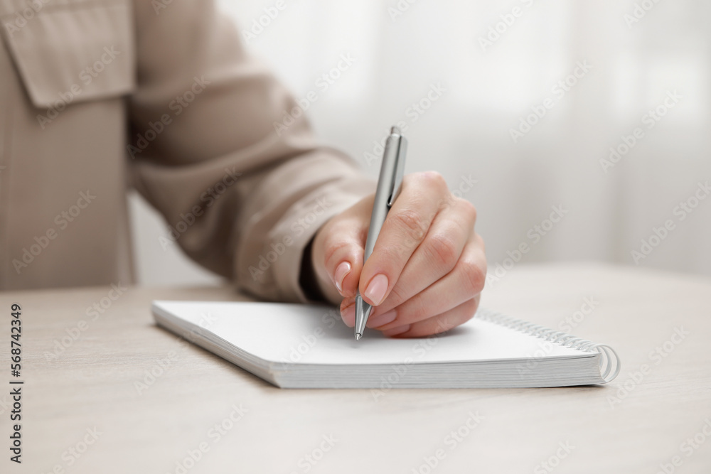 Fototapeta premium Woman writing in notebook at wooden table, closeup