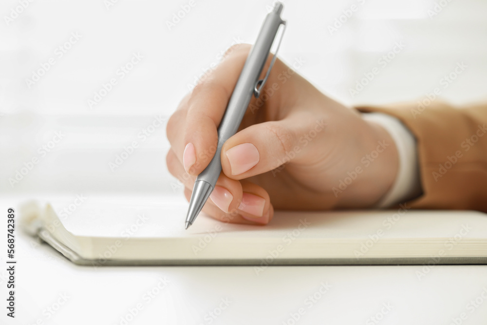 Woman writing in notebook at white table, closeup Woman writing in notebook at white table, closeup