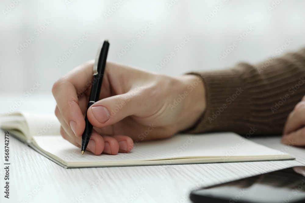 Man writing in notebook at white wooden table, closeup Man writing in notebook at white wooden table, closeup